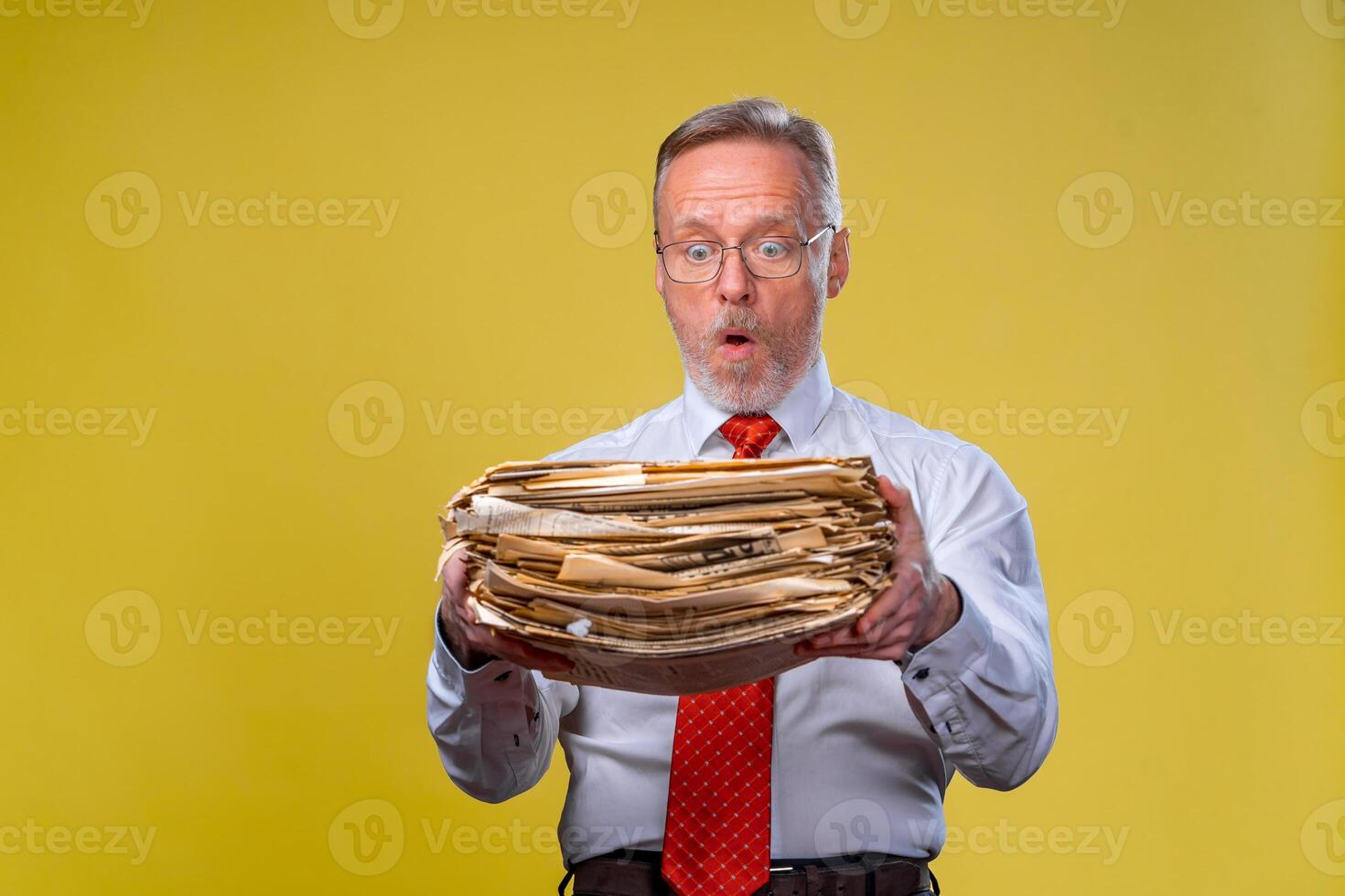 Frustrated executive worker over yellow background overworked holdind piles of documents paper work photo