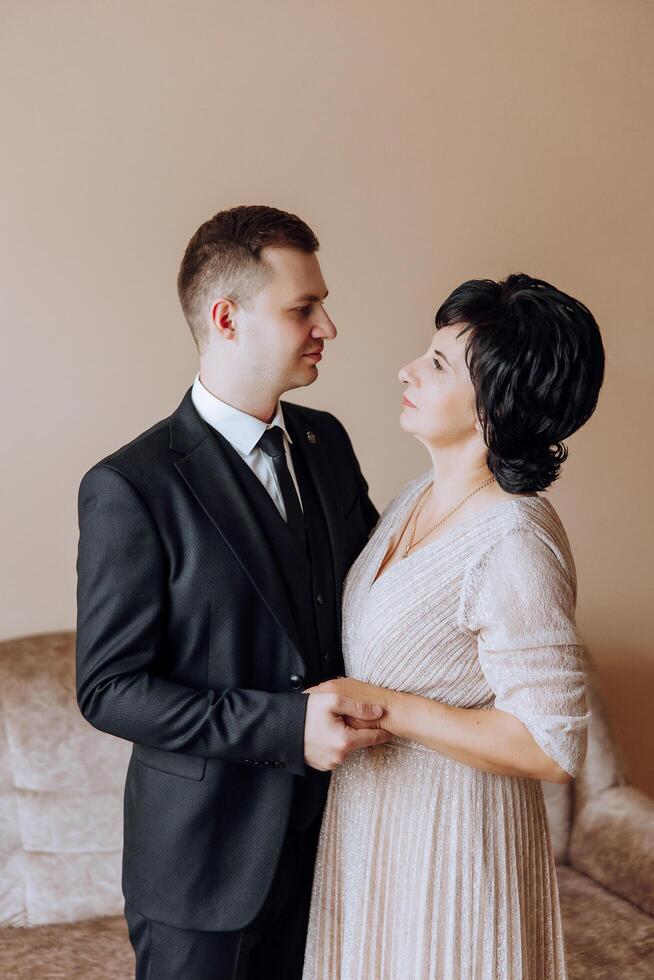 mother helps her adult son prepare for the wedding ceremony. An emotional and touching moment at a wedding. A mother hugs her son photo