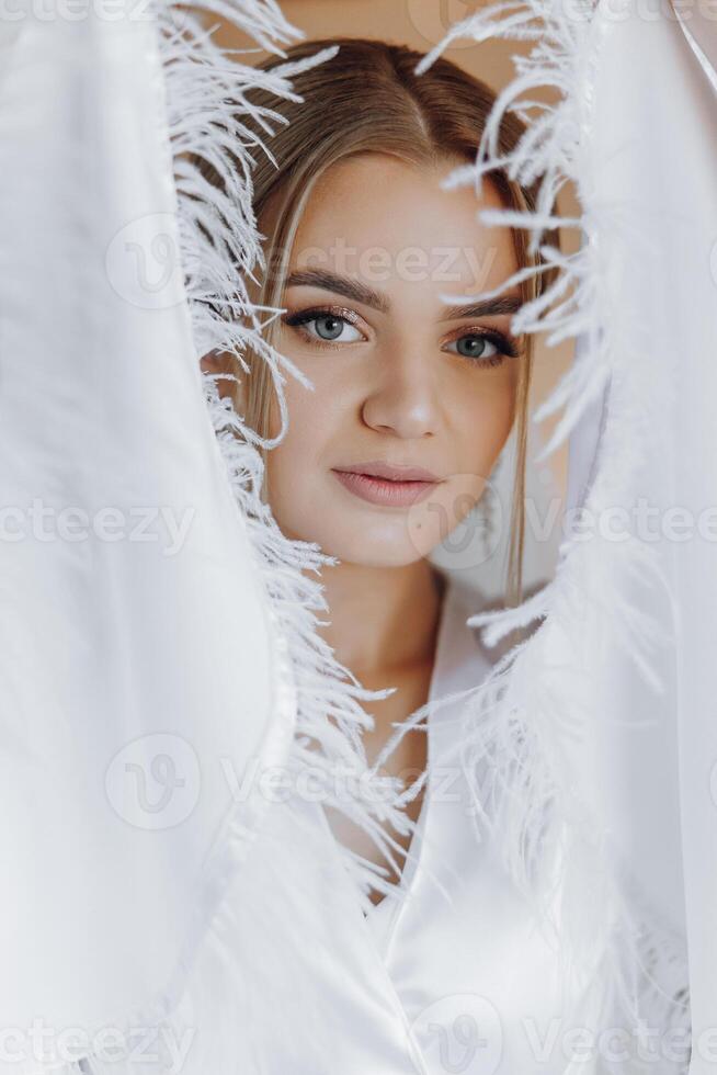 portrait of an incredibly beautiful girl bride in a white robe in the bedroom, the bride poses in the morning before the wedding ceremony. photo