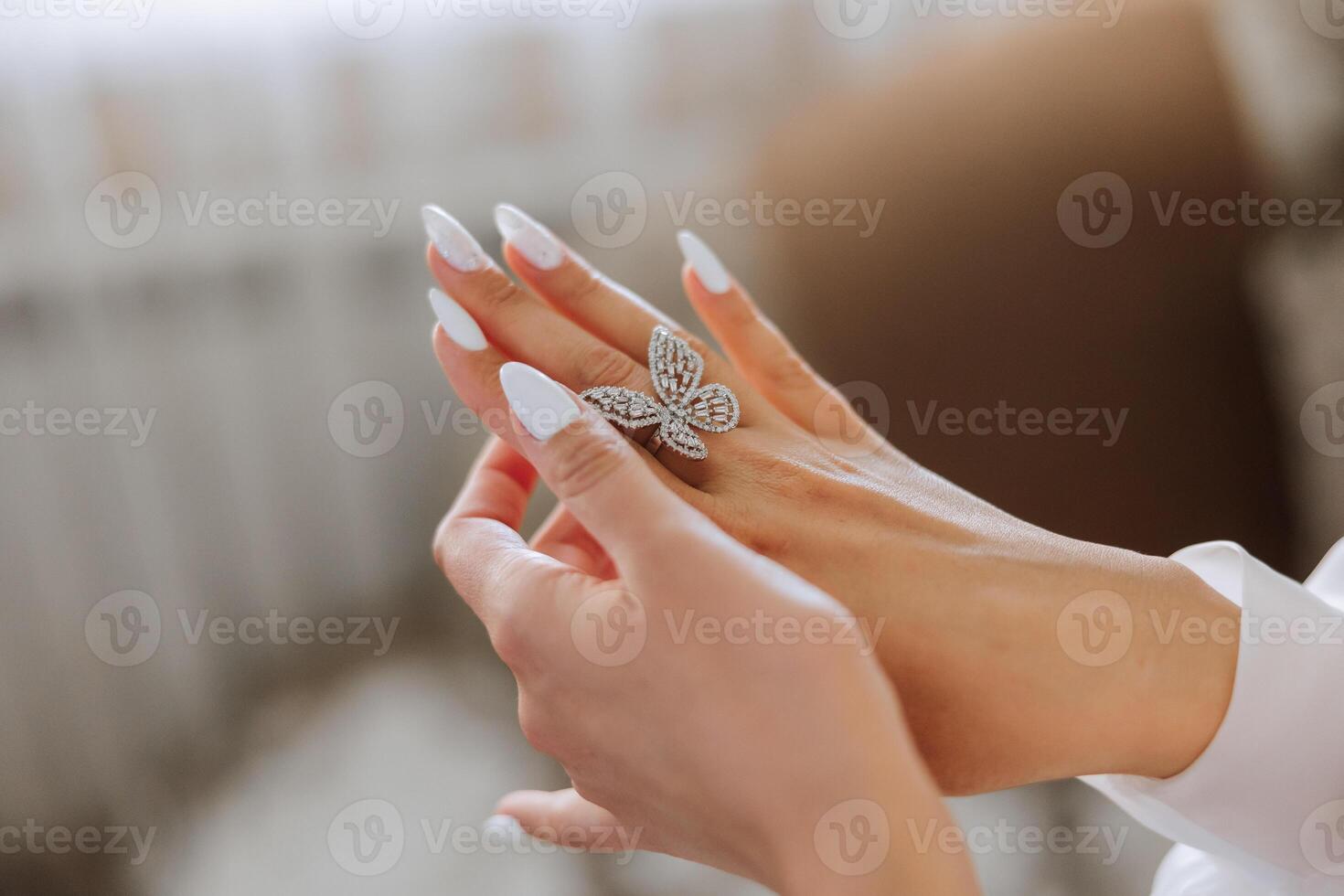 Close-up of an elegant diamond ring in the form of a butterfly on the finger of a woman with a modern manicure, sunlight. Love and wedding concept. Soft and selective focus. photo