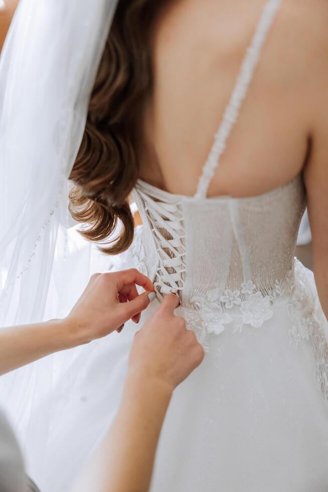 The bride's friend helps her get dressed in a white wedding dress in the morning. wedding morning, blurred focus. A friend of the bride helps to tie her wedding dress. photo