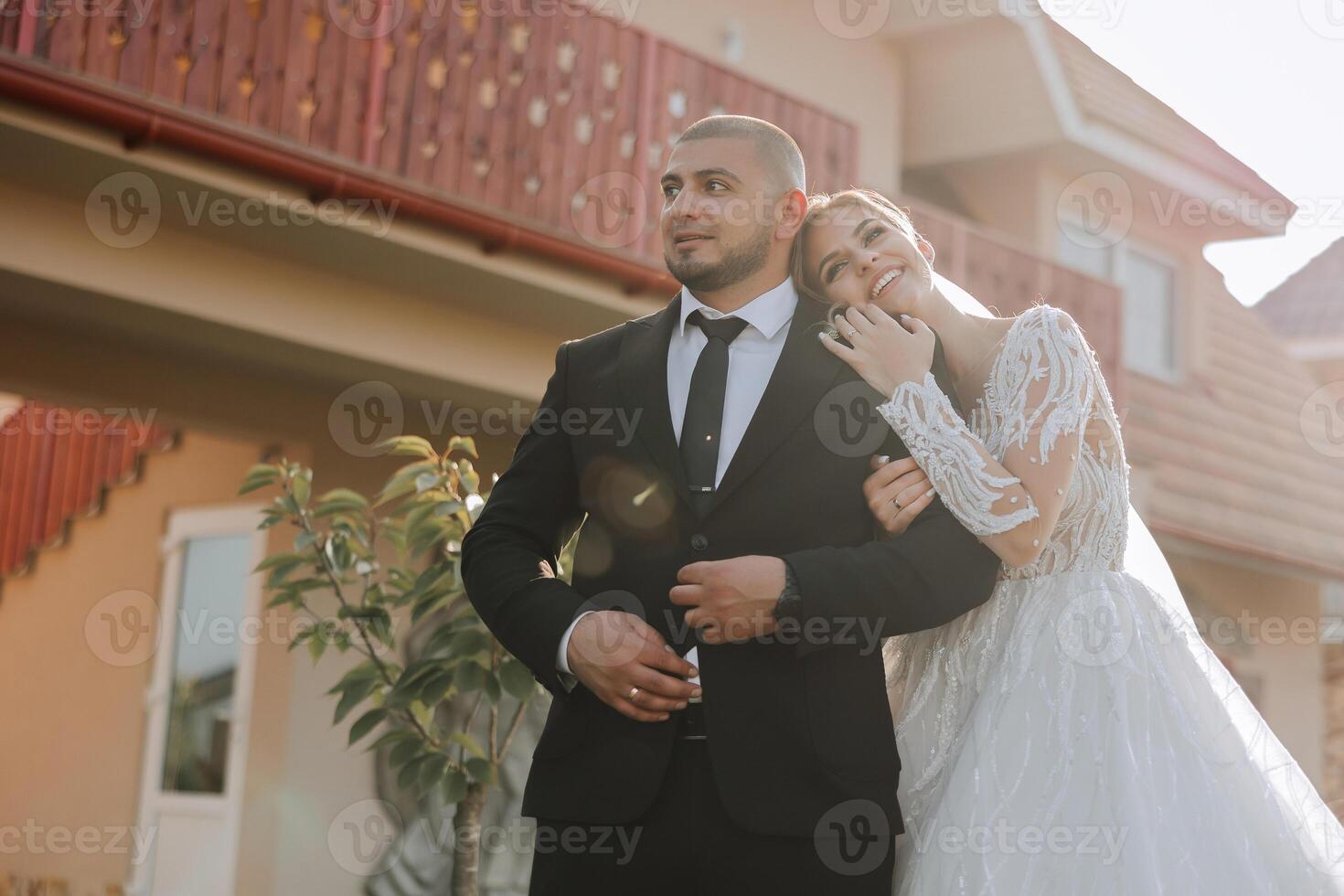 lovely and stylish newlyweds are hugging and smiling against the background of autumn nature in a beautiful garden. An incredibly beautiful young bride leaned against the shoulder of her beloved groom photo