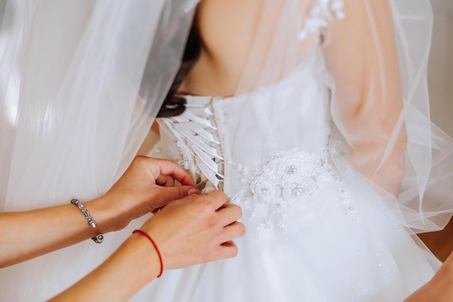The bride's friend helps her get dressed in a white wedding dress in the morning. wedding morning, blurred focus. A friend of the bride helps to tie her wedding dress. photo