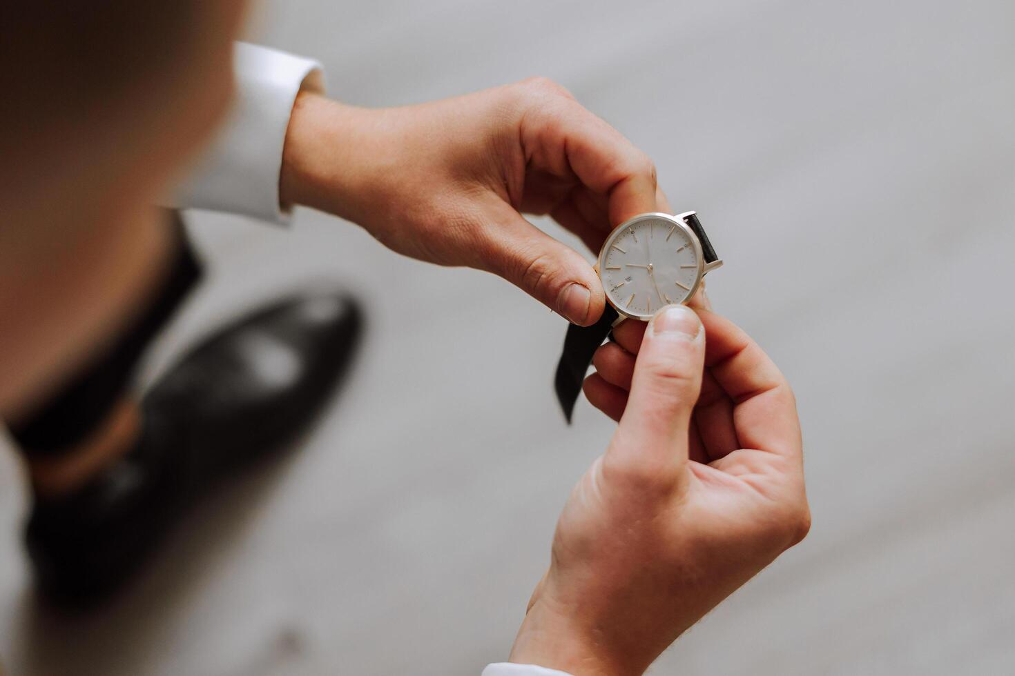 A close-up of a cropped frame of a man puts on a watch with a leather belt, is dressed in a stylish suit, a white shirt, wears a gold ring. photo
