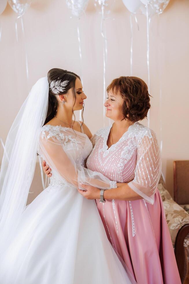 A beautiful and happy mother and her daughter, the bride, are standing next to each other. The best day for parents. Tender moments at the wedding. photo