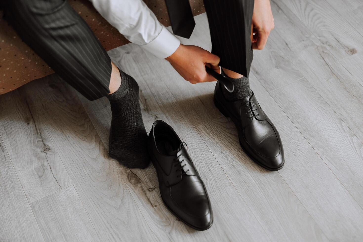 A man is putting on his shoes while sitting on a sofa in a hotel room. A young entrepreneur is preparing to go on a business trip. Businessman preparing for travel in home bedroom early in the morning photo