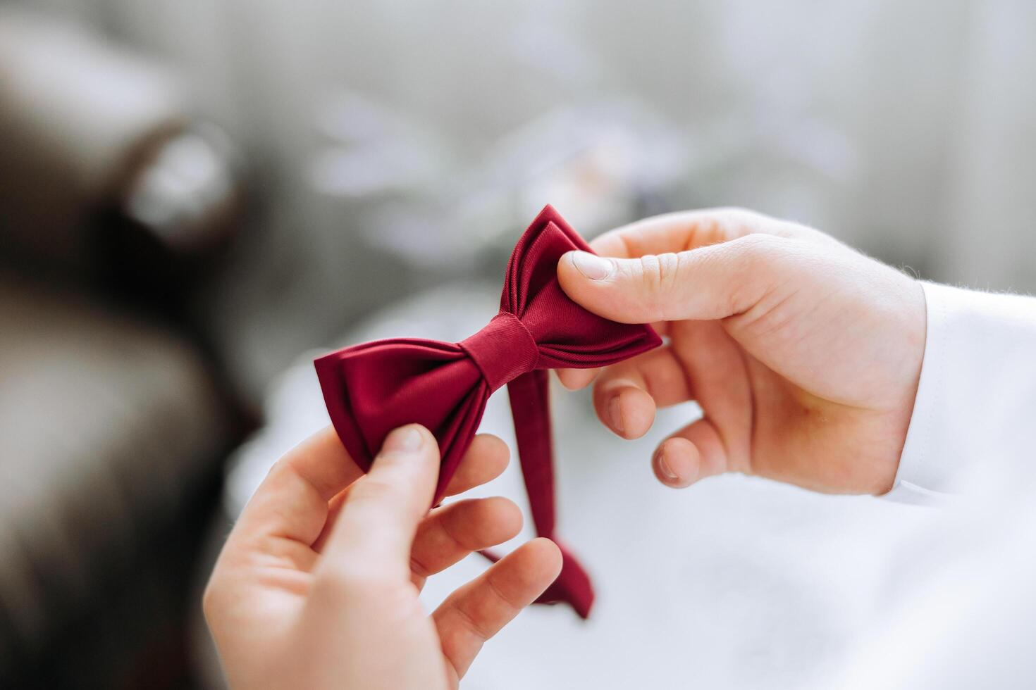 a young man in a white shirt stands by the window in the room and puts on a tie. The groom gets dressed in the morning and prepares for the wedding. photo