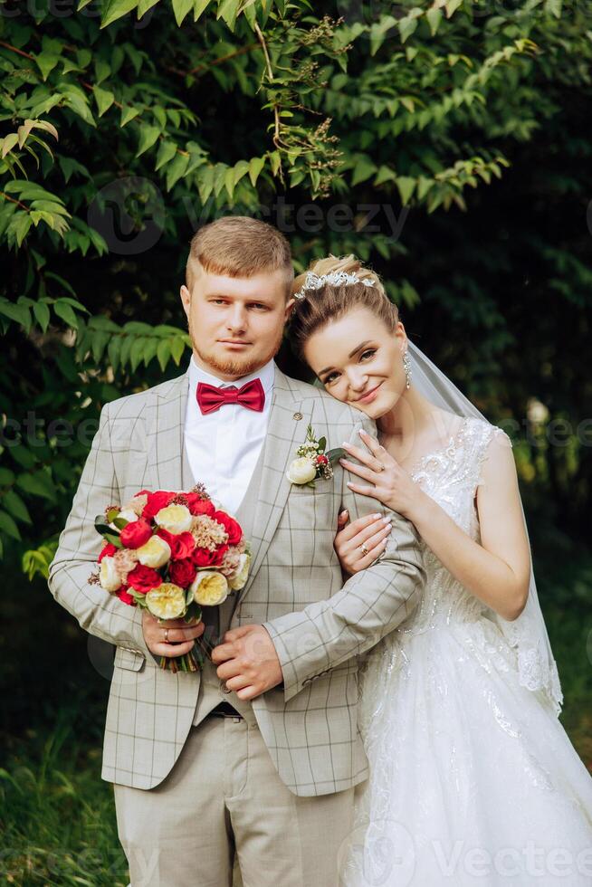 lovely and stylish newlyweds are hugging and smiling against the background of autumn nature in a beautiful garden. An incredibly beautiful young bride leaned against the shoulder of her beloved groom photo