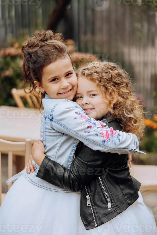 Two little girls hug, friendship. Two little sisters in beautiful dresses are hugging in the yard. Happy childhood. photo