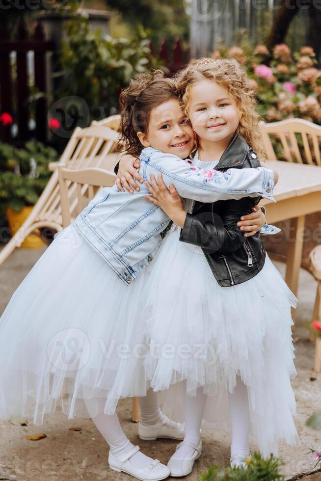 Two little girls hug, friendship. Two little sisters in beautiful dresses are hugging in the yard. Happy childhood. photo