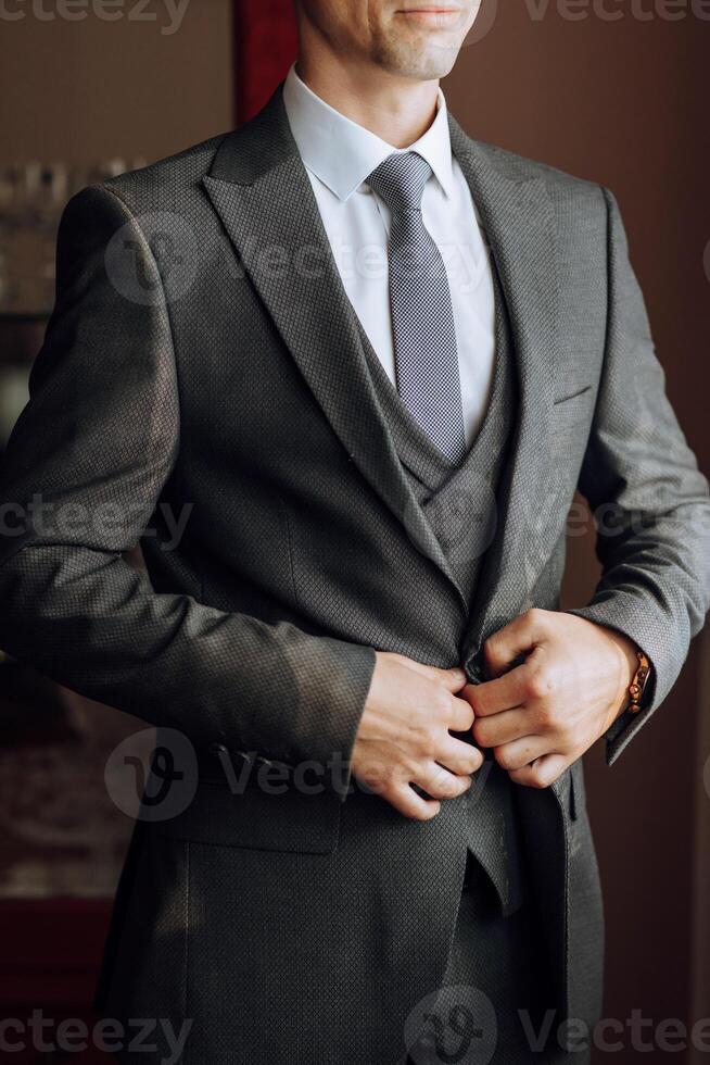 the groom's hands fasten his jacket in the morning before the wedding. close-up of a man in business suit. Businessman puts on a suit. The man fastens the buttons on his jacket. photo