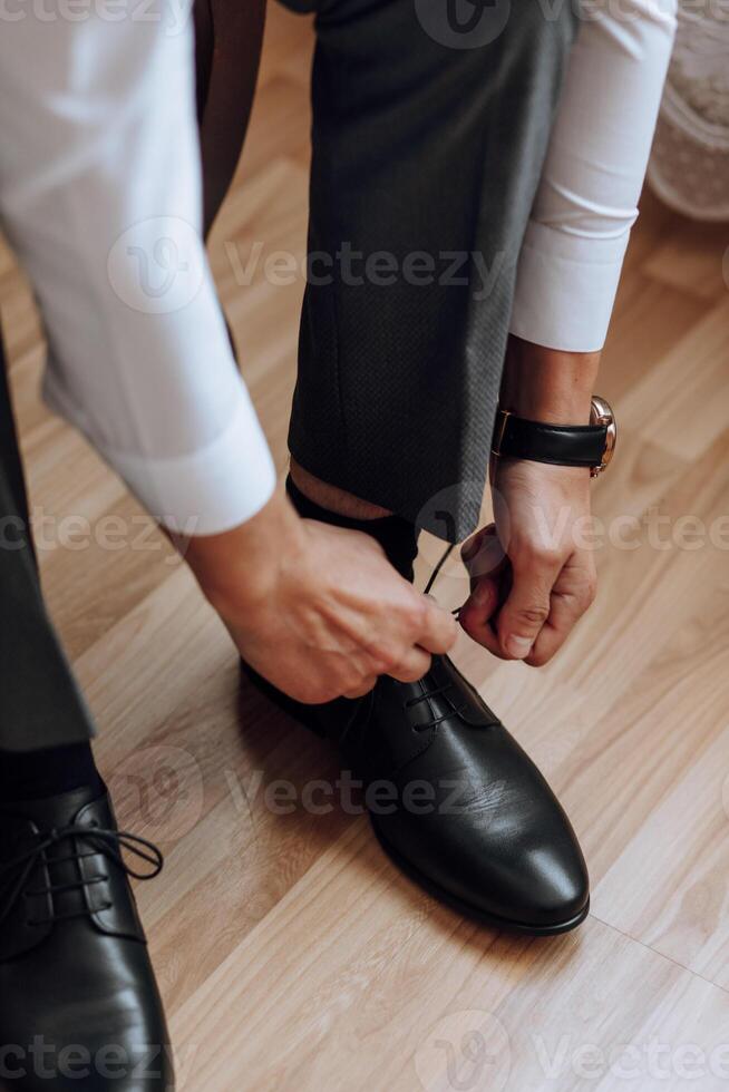 A man is putting on his shoes while sitting on a sofa in a hotel room. A young entrepreneur is preparing to go on a business trip. Businessman preparing for travel in home bedroom early in the morning photo