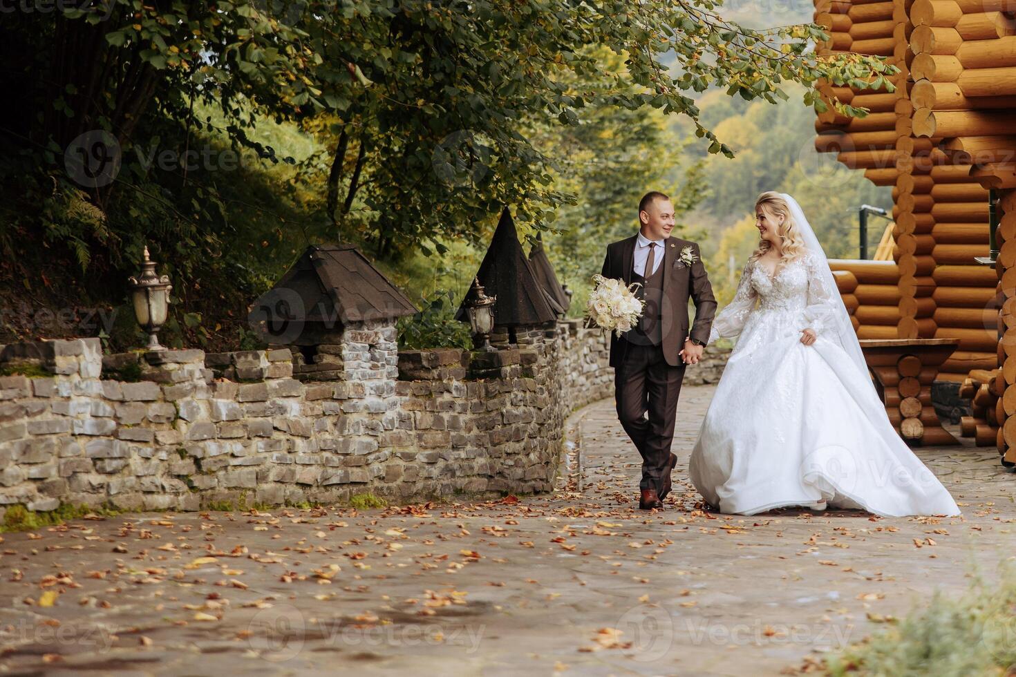 A wedding couple is walking in nature on an autumn day. Happy young bride and elegant groom holding hands. A stylish couple of newlyweds on their wedding day. photo