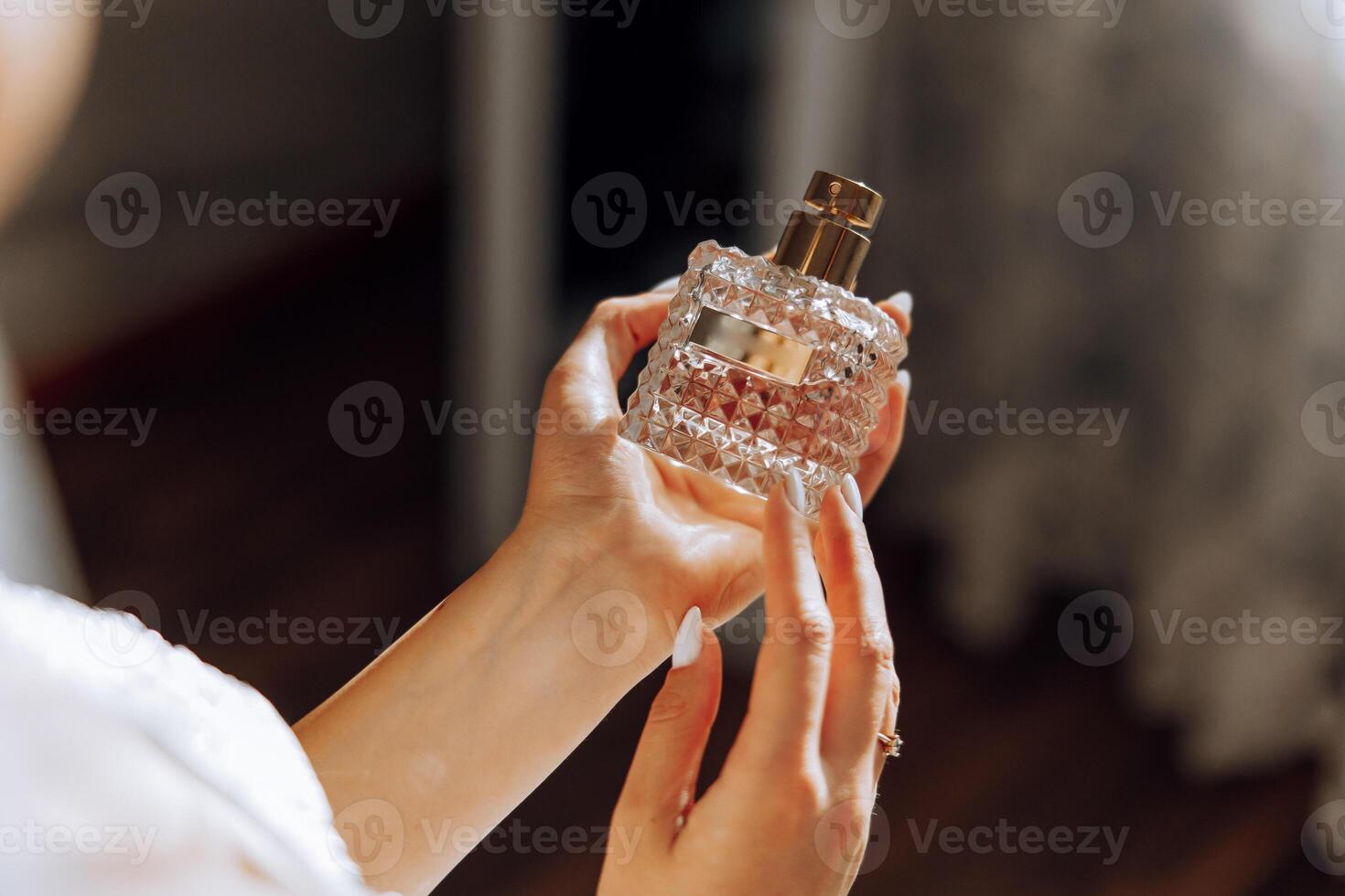 Glass bottle of perfume in gentle female hands. The bride sprays perfume on her body. Close-up photo. Manicure. Morning of the bride. photo