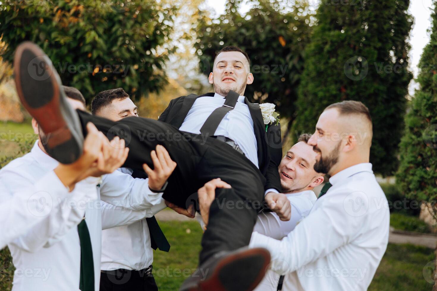 Wedding photo session in nature. Friends hold the groom in their arms