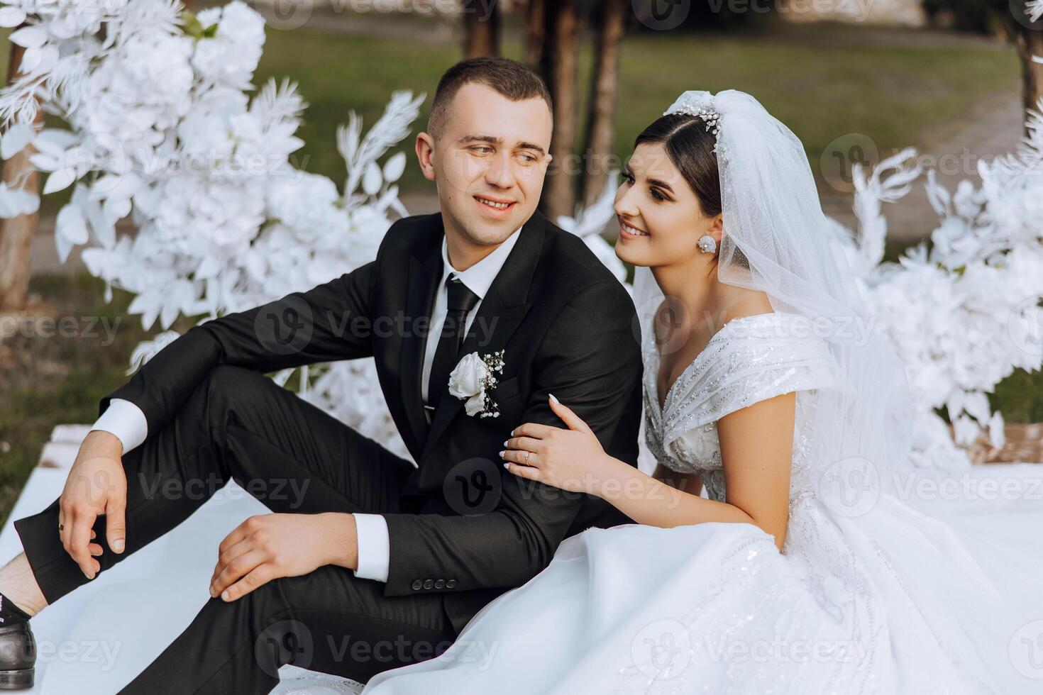 lovely and stylish newlyweds are hugging and smiling against the background of autumn nature in a beautiful garden. An incredibly beautiful young bride leaned against the shoulder of her beloved groom photo