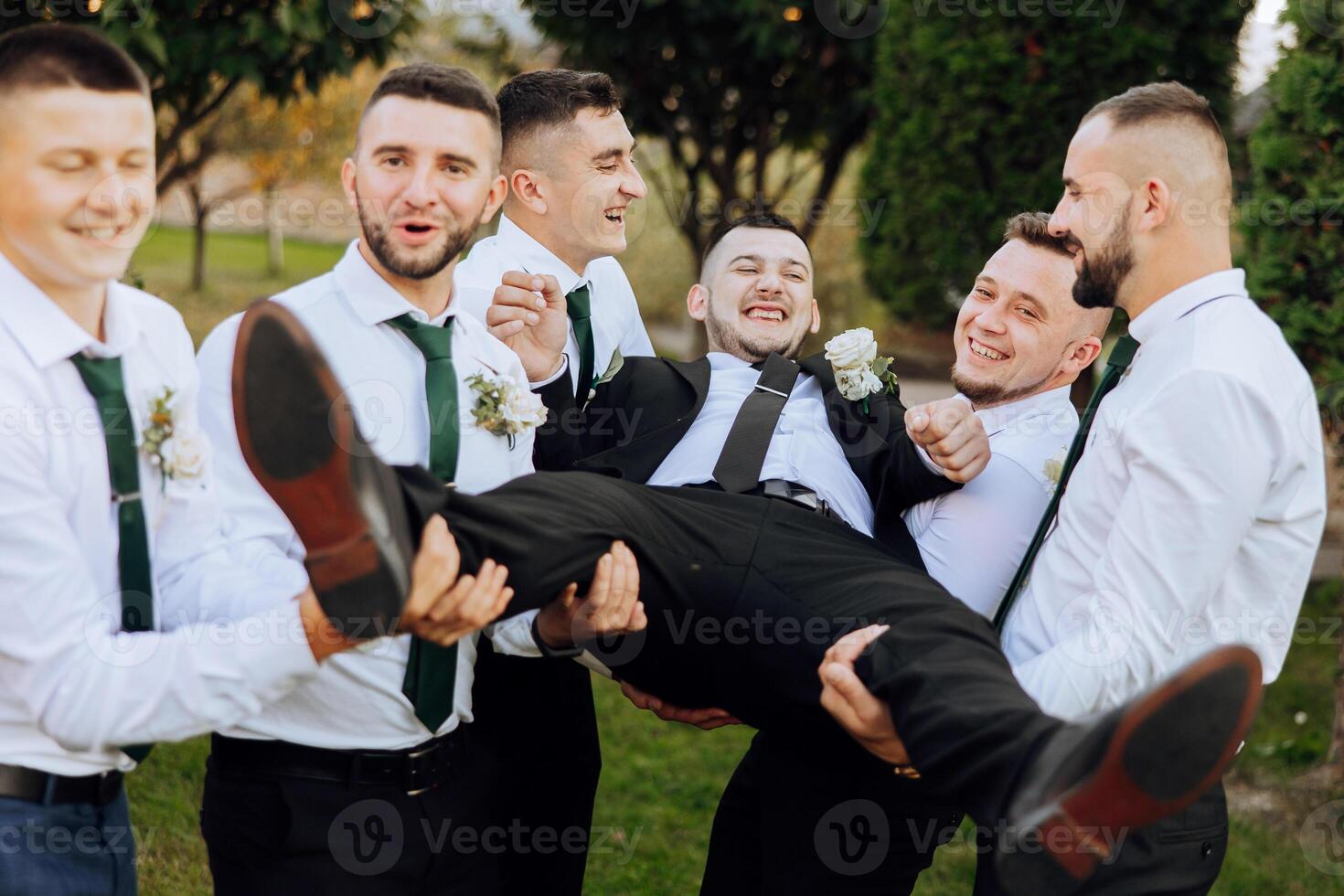 Wedding photo session in nature. Friends hold the groom in their arms