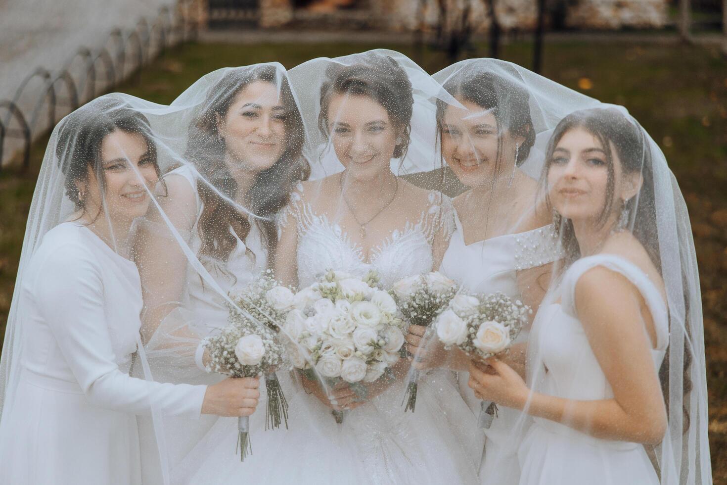 Boda fotografía en naturaleza. un morena novia y su novias actitud debajo un velo, participación ramos de flores foto