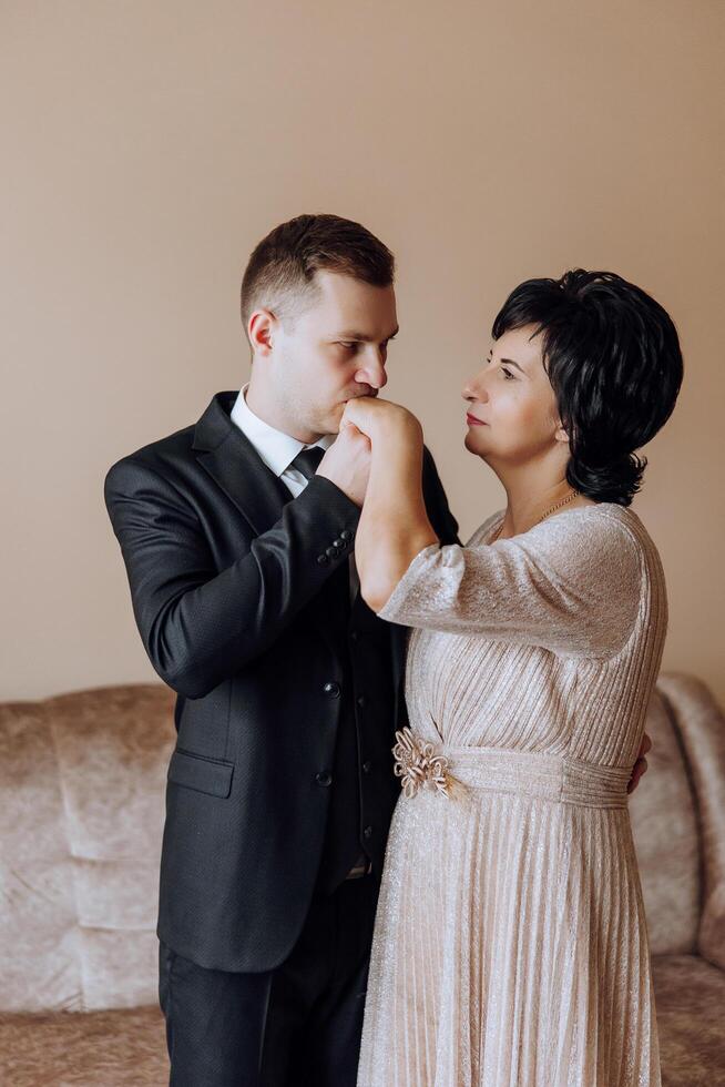 mother helps her adult son prepare for the wedding ceremony. An emotional and touching moment at a wedding. A mother hugs her son photo