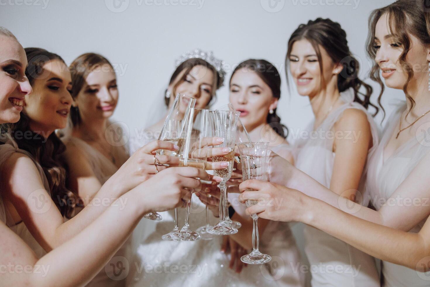 Photo with bridesmaids drinking champagne from glasses in the morning in a beautiful hotel. Photo of a beautiful young bride and her friends in matching dresses drinking champagne before the wedding.