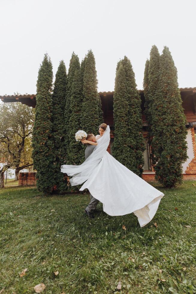 hermoso novio que lleva un hermosa riendo novia en su brazos en un primavera parque. el novio es dando vueltas con el novia en su brazos foto