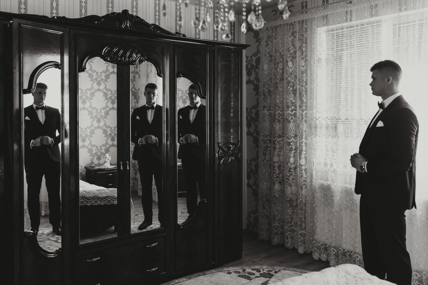 black and white photo. A handsome man in a black suit poses in front of the camera, reflected in the mirror. Side view. Daylight. Fashion and style. Business. Men's style. Beautiful hands photo