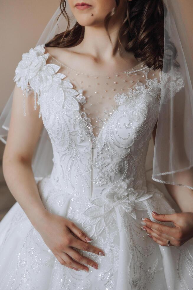 The bride's wedding dress with sleeves. The dress is embroidered with beads and the sleeves are made of veil. Close-up photo