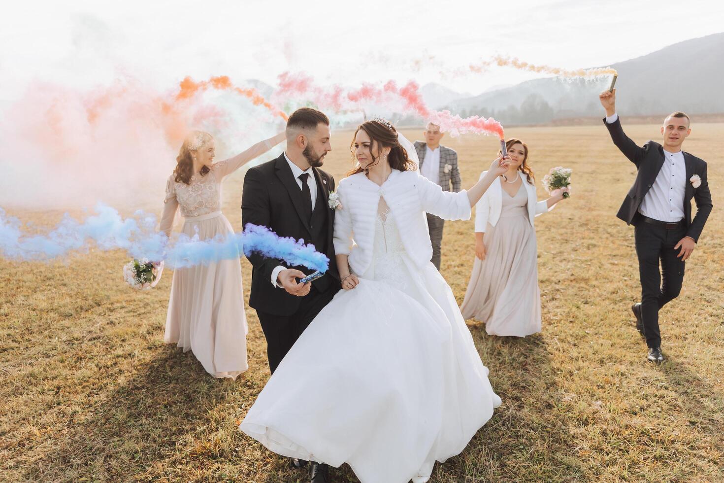 Wedding photo session in nature. Bride and groom and their friends in a field, cheerfully holding colored smoke.