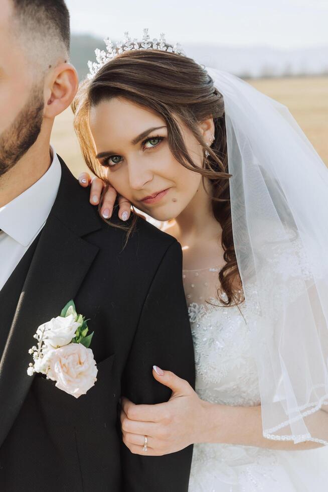 cute and stylish newlyweds are hugging and smiling against the background of autumn nature in a beautiful garden. An incredibly beautiful young bride kisses her lover photo