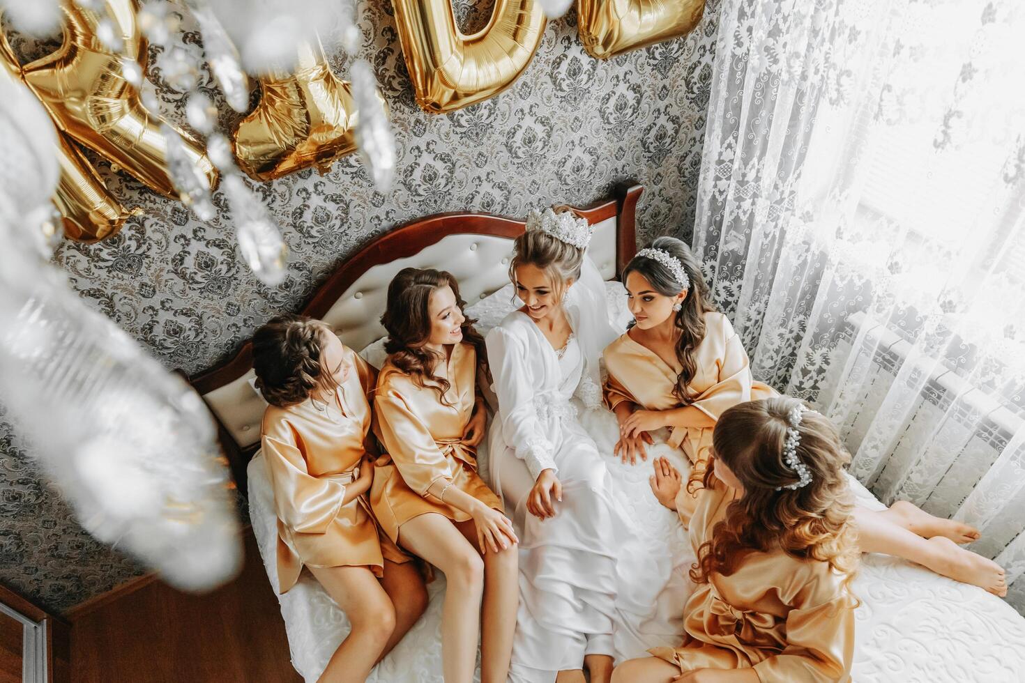 joven damas de honor en seda batas en un hotel habitación. hermosa mujer celebrando un despedida de soltera fiesta sentado en el cama en temática pijama. foto