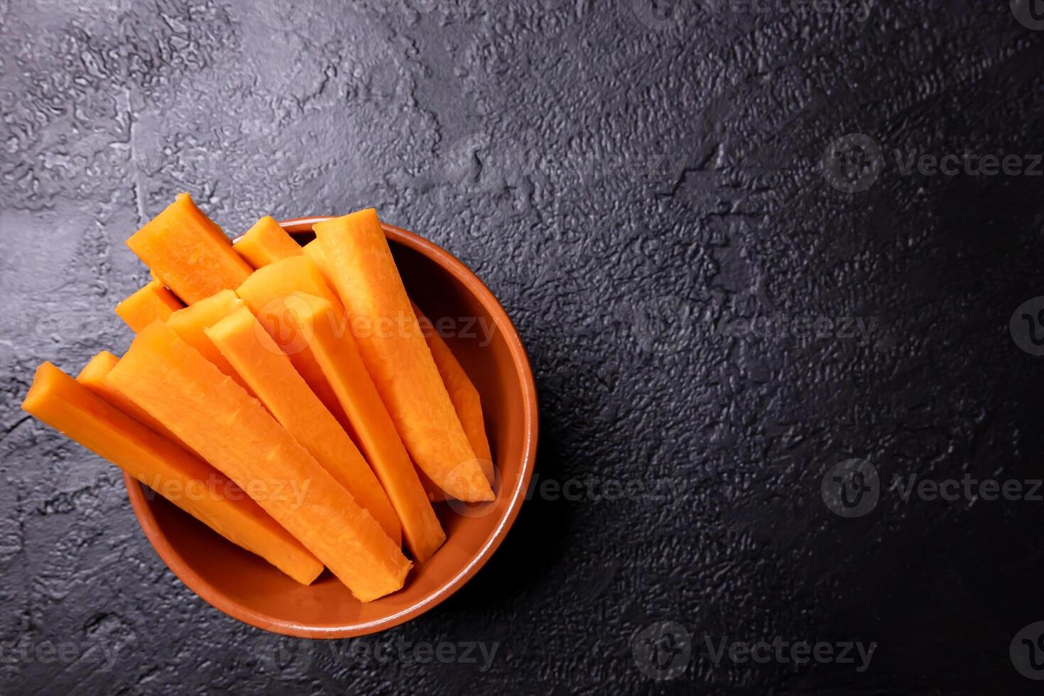 Carrot pieces on a dark background inside a bowl. photo