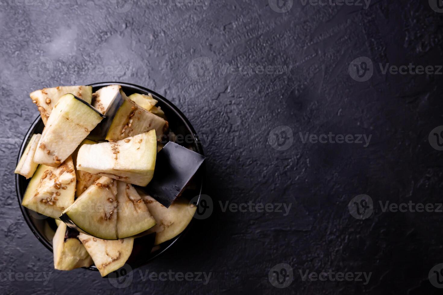 Pieces of eggplant inside a bowl on a very dark background. photo