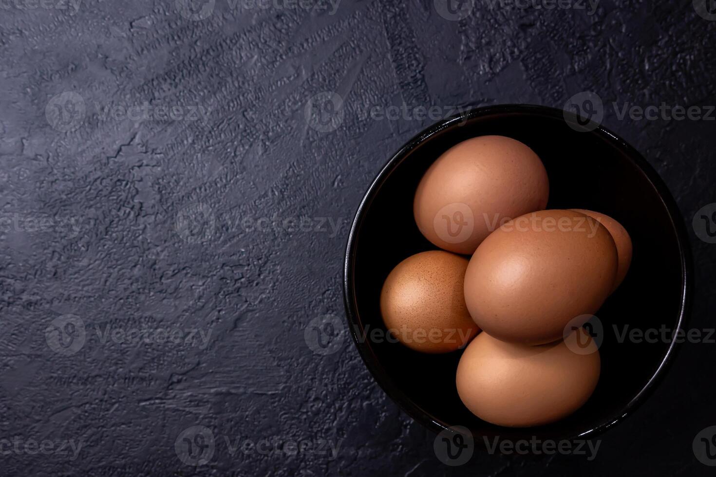 Fresh eggs in a bowl on a dark colored table. photo