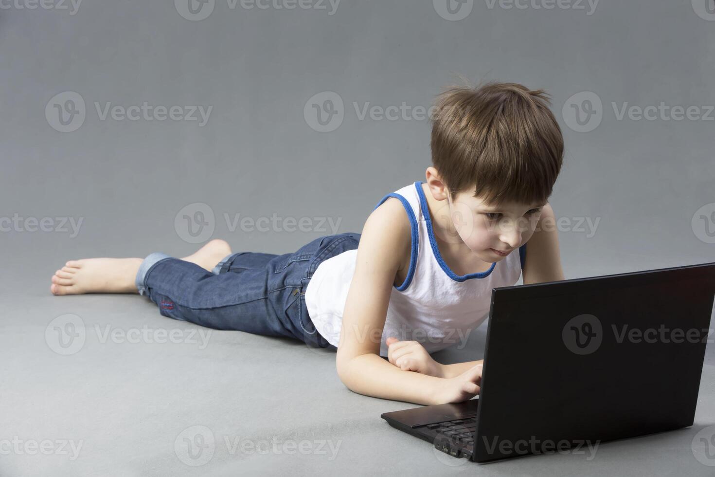 Child with a computer. The boy is lying on the floor with a laptop photo