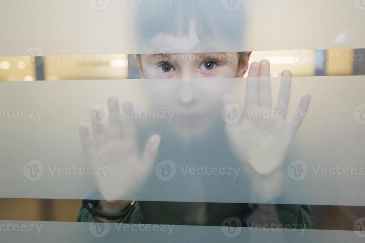 The child is looking through the glass. Boy peeps in frosted glass photo