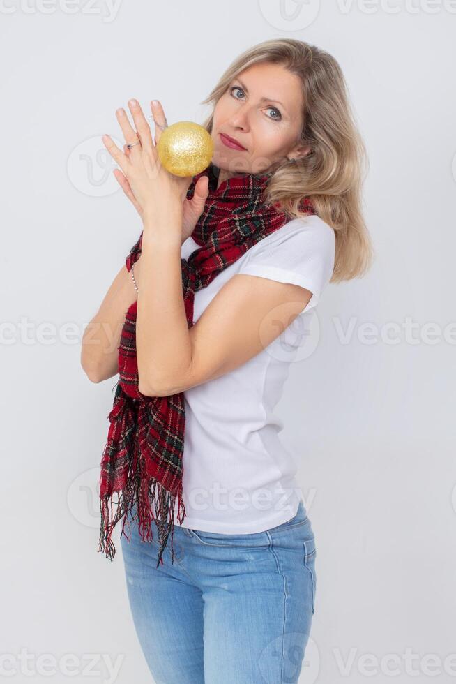 un hermosa adulto mujer en un a cuadros bufanda sostiene un Navidad oro pelota. foto