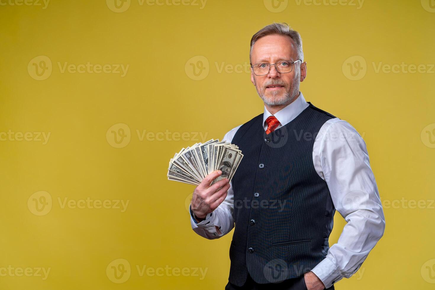 antiguo sonriente canoso hombre en los anteojos participación ventilador de dolares en mano. contento sonrisa en un rostro. mucho dinero facturas. humano emociones y facial expresiones foto