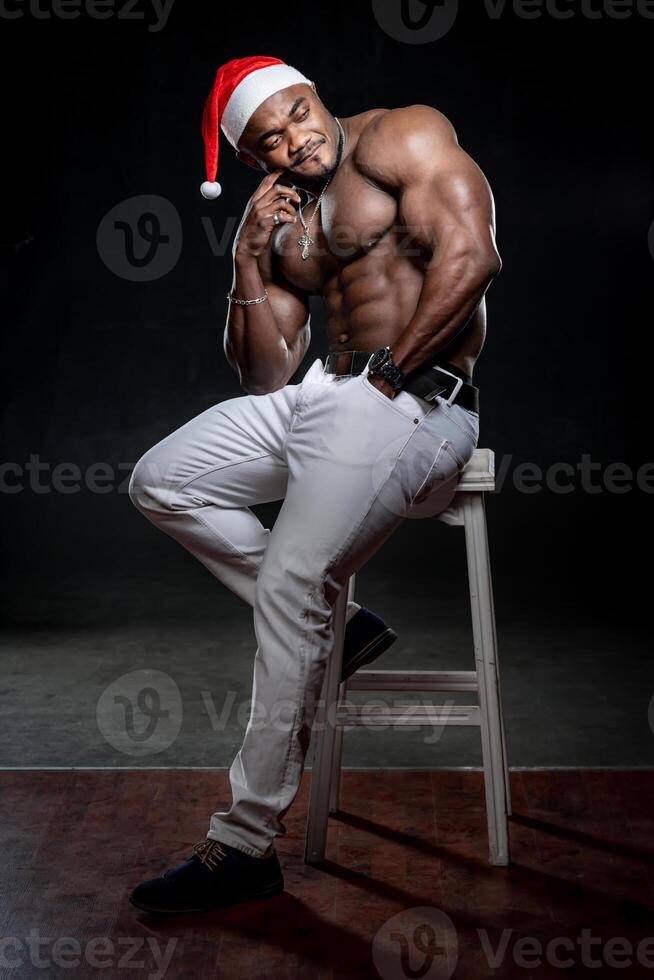 Sexy handsome male posing for camera. Athletic model in Christmas hat looking away during the shooting in studio photo