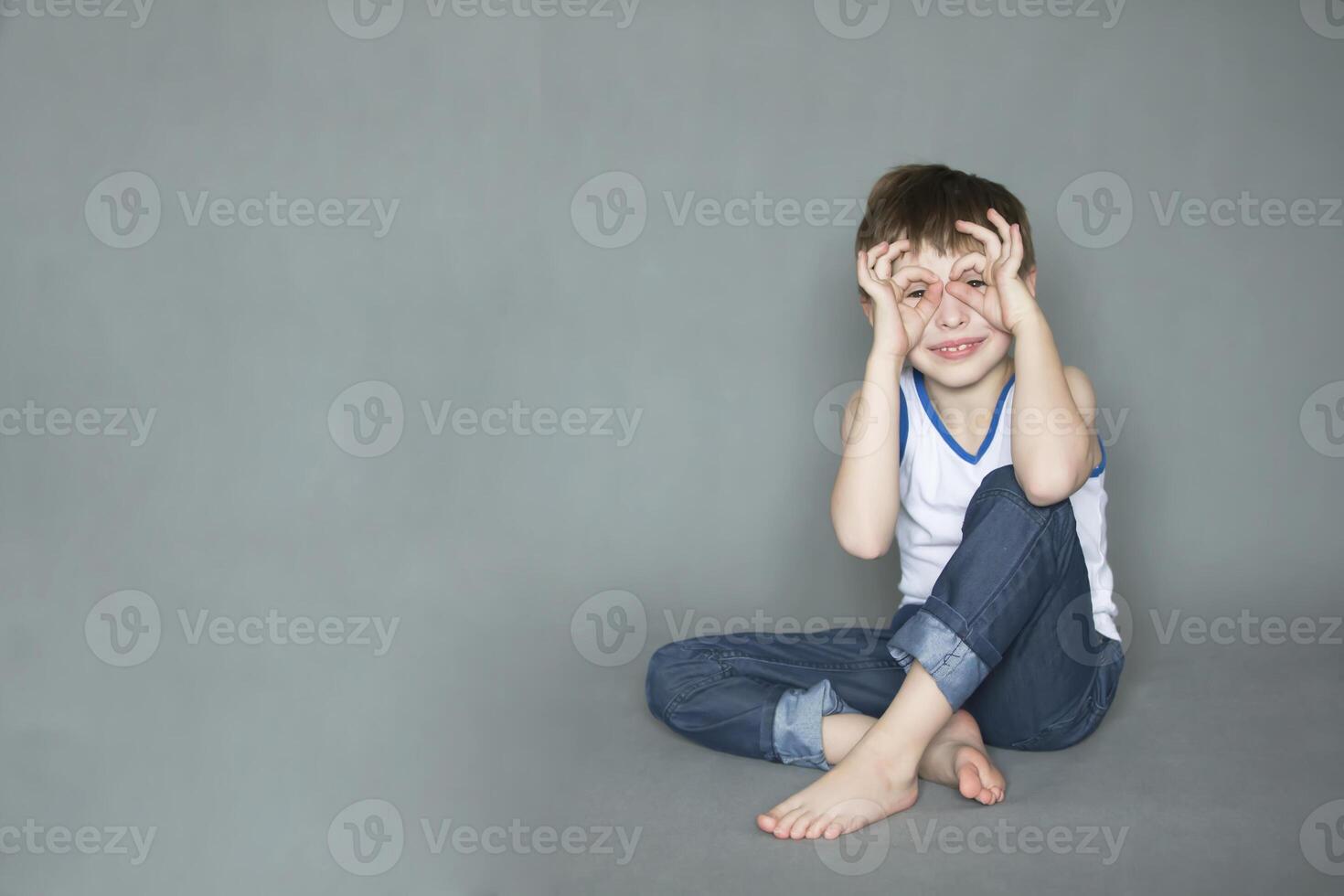 Comic happy boy holding his fingers near the eyes like glasses. Cheerful seven eight year old child. photo