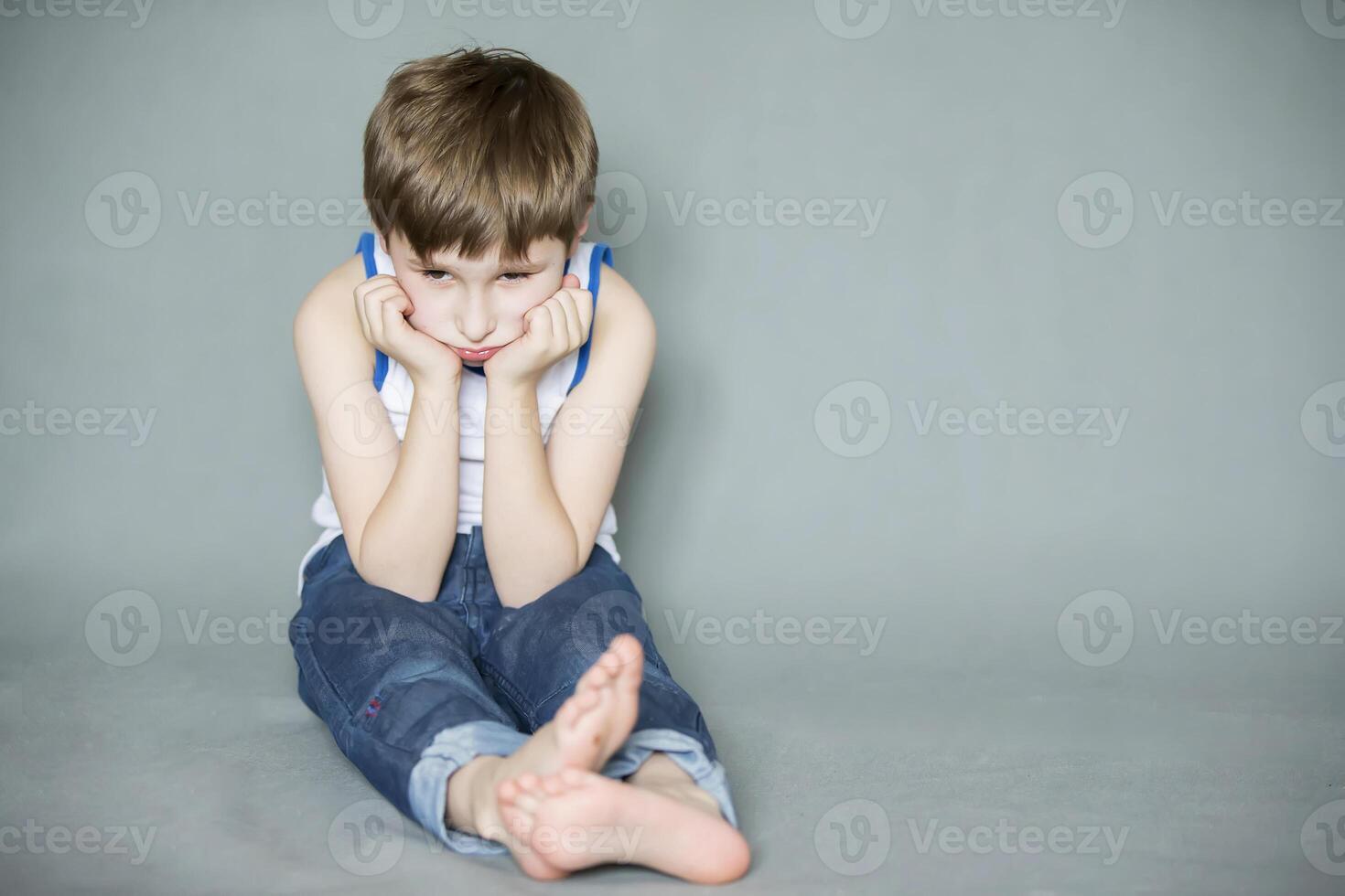 Sad preschooler sitting on the floor. A bored child. Upset little boy. photo