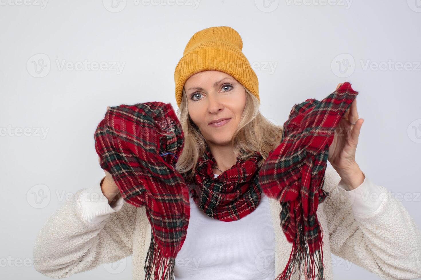 Close-up portrait of an elderly woman in a knitted hat, wrapped in a scarf against the cold on a gray background photo