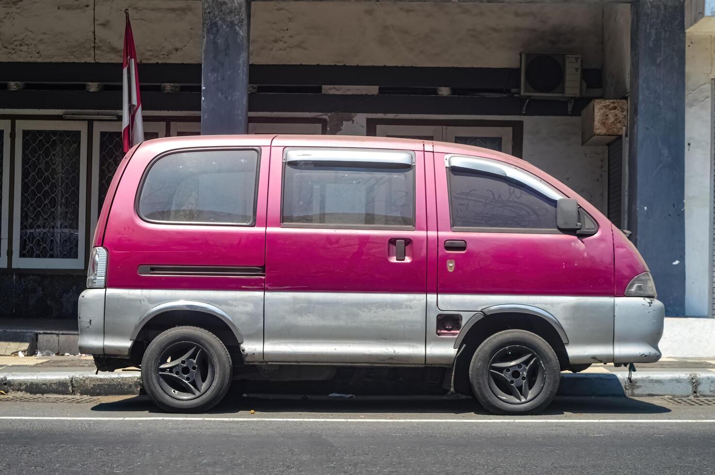 an old red car parked on the side of an urban highway, Indonesia, 17 September 2023. photo
