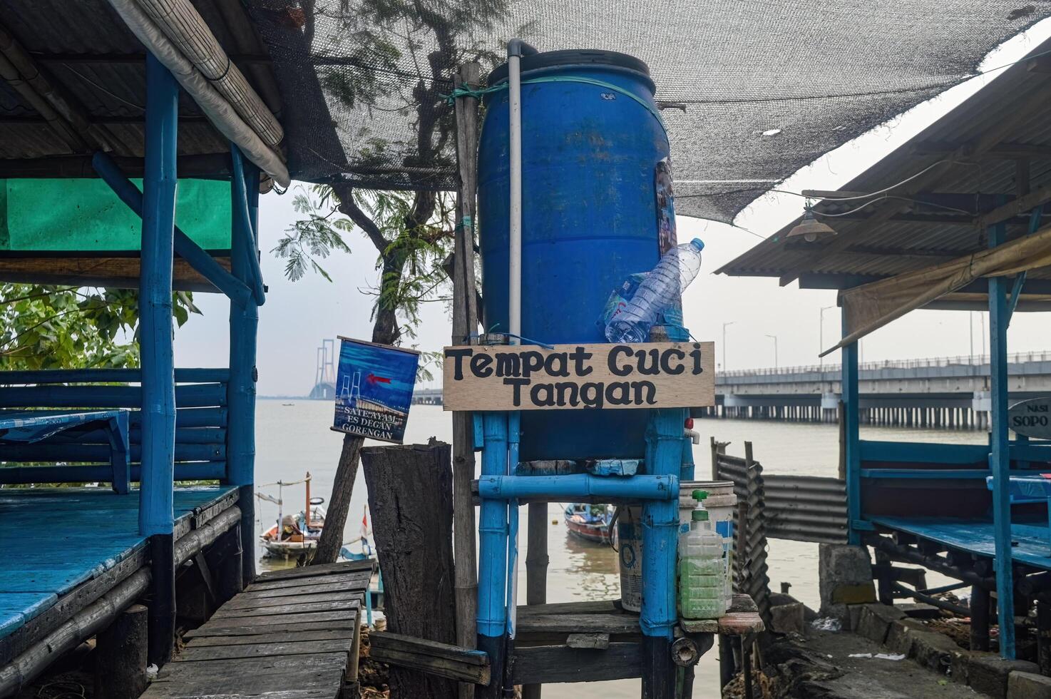 A simple hand washing place made from plastic drums and bamboo in a traditional restaurant in Madura with the Suramadu bridge in the background, indonesia, 17 November 2023. photo