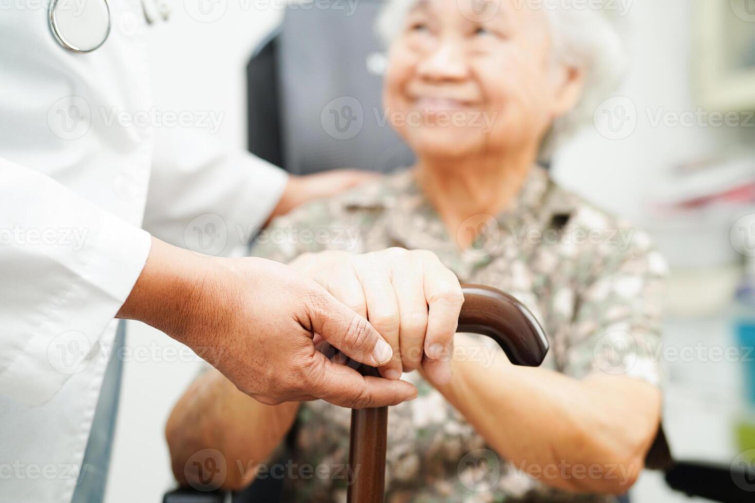 Doctor help Asian elderly disability woman patient holding walking stick in wrinkled hand at hospital. photo
