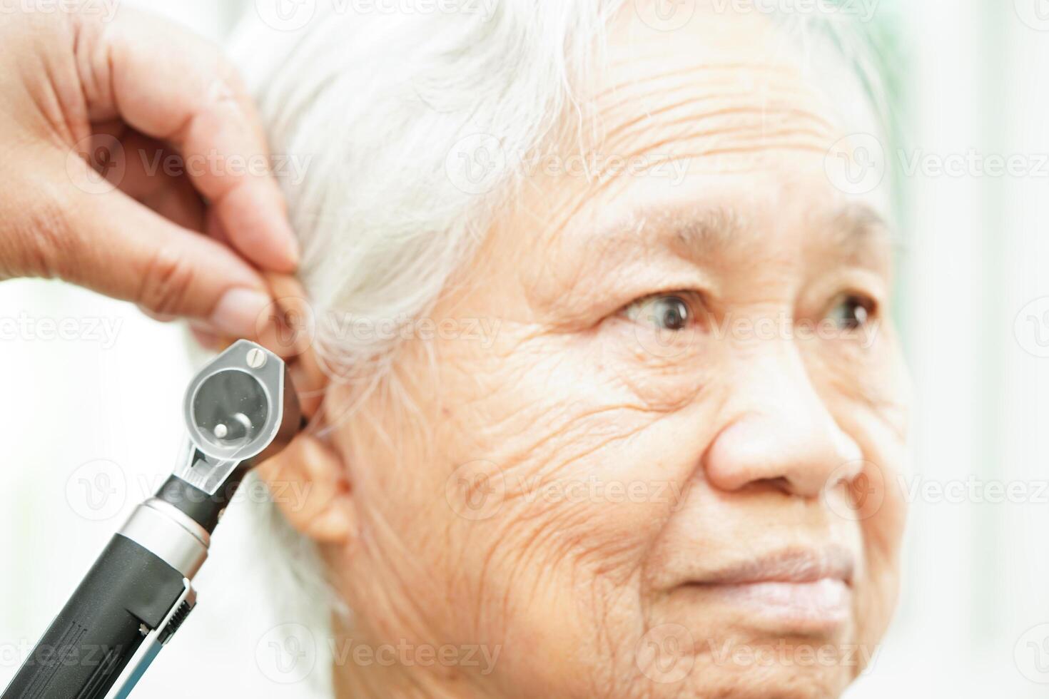 Otolaryngologist or ENT physician doctor examining senior patient ear with otoscope, hearing loss problem. photo