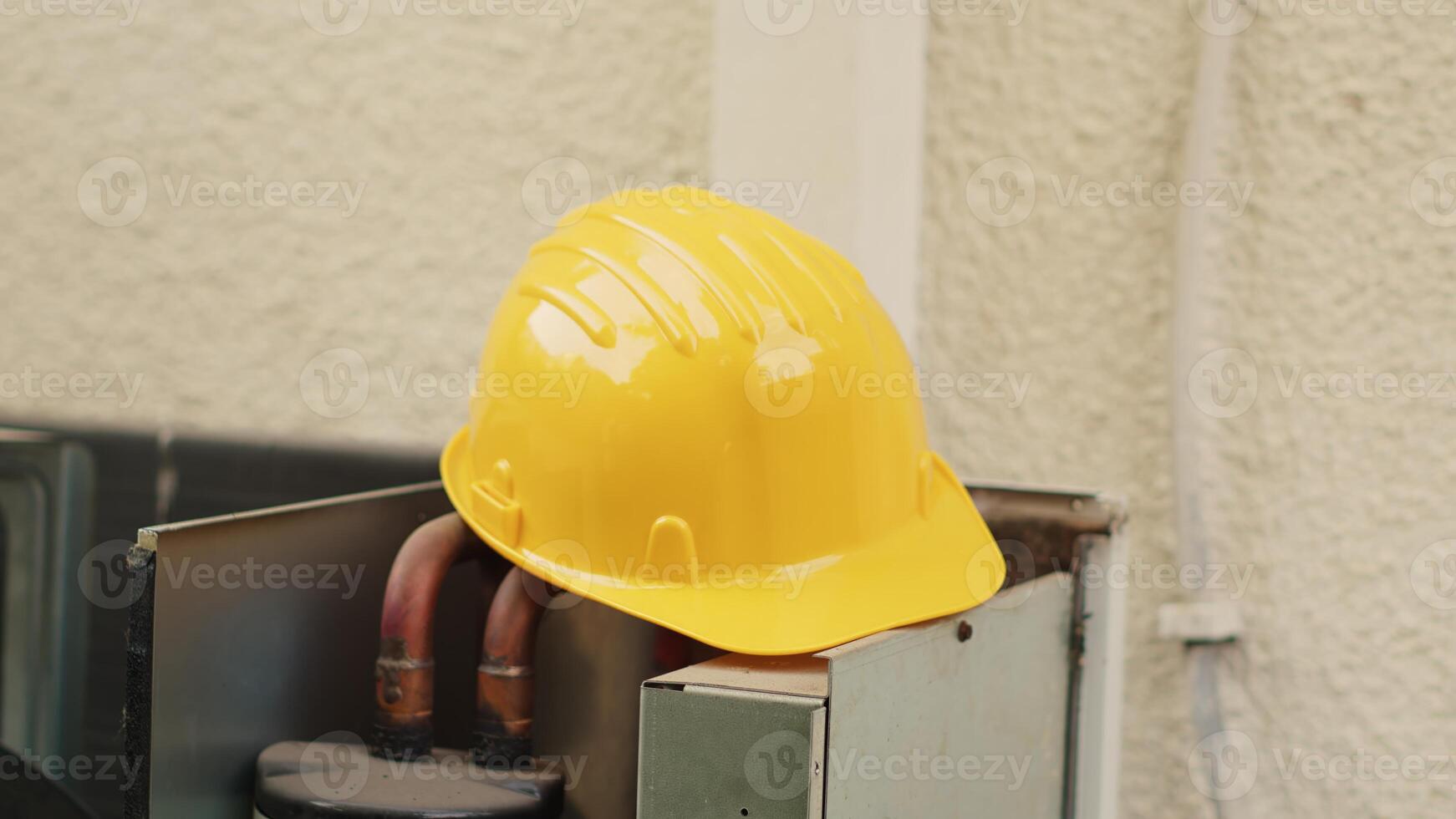 Extreme close up of yellow safety hardhat on top of out of order external air conditioner unit in need of repair. Protective professional engineering gear left on opened HVAC system photo