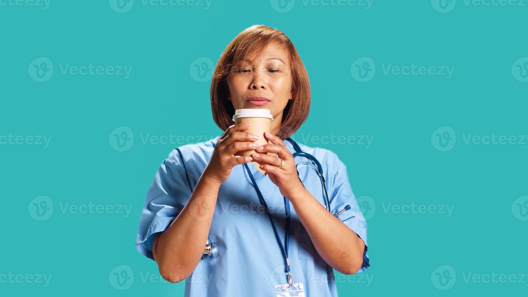 BIPOC nurse tasting instant coffee while at work, surprised by unexpected aroma. Close up shot of hospital employee drinking hot beverage with unusual aftertaste, isolated over studio background photo
