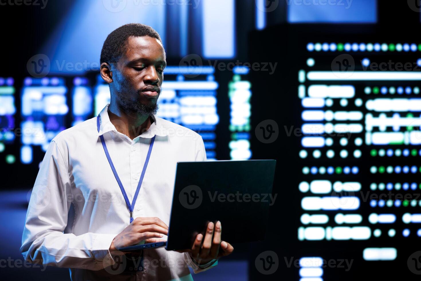 IT programmer in server hub using laptop to find network issues affecting supercomputer performance. Employee fixing issues leading to slow data transfer rates and poor client communication photo