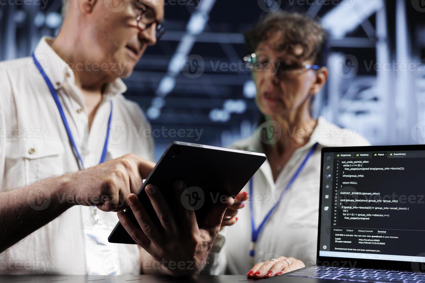 Octogenarian cloud computing company executives updating blade servers, writing intricate binary code scripts on tablet and laptop, using programming to fortify cybersecurity in data center photo