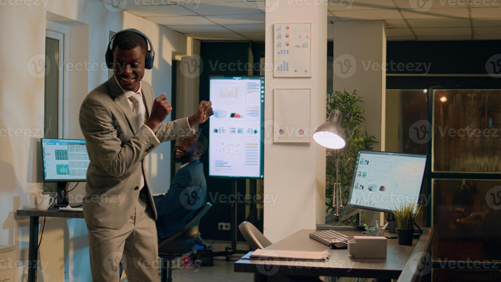Employee dancing while enjoying music at work, tired of working on computer. Businessman showing exquisite dance moves, spinning around in office, making coworker laugh during nightshift photo
